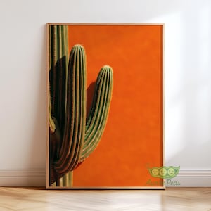 May include: A framed art print featuring a close-up of a green cactus against a vibrant orange background. The cactus has vertical ridges and small spines. The wooden frame adds a natural touch to the desert-themed artwork.