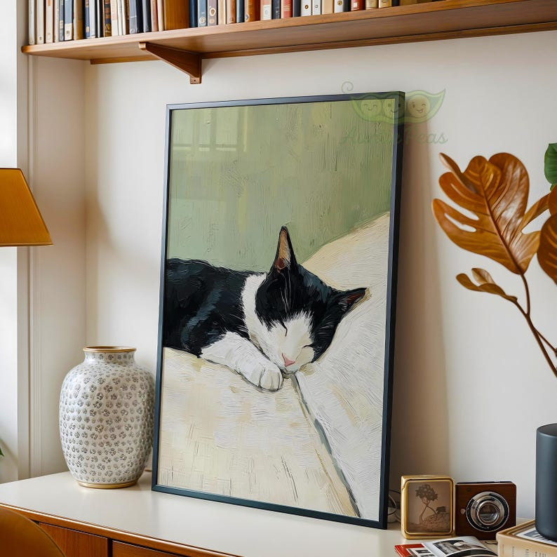May include: Framed art print featuring a sleeping black and white cat. The cat is resting on a white surface against a light green background. The artwork is displayed in a black frame and is a charming addition to any home decor.
