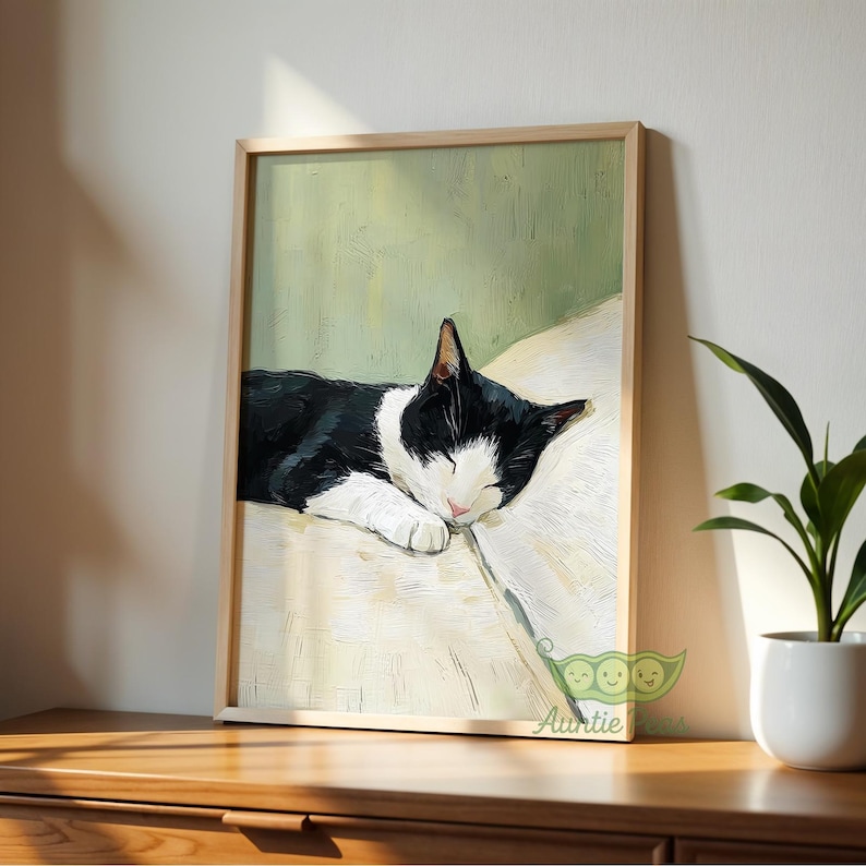 May include: A framed art print featuring a sleeping black and white cat. The cat is resting on a cream-colored surface against a light green background. The artwork is displayed in a light-colored wooden frame, creating a serene and calming aesthetic.