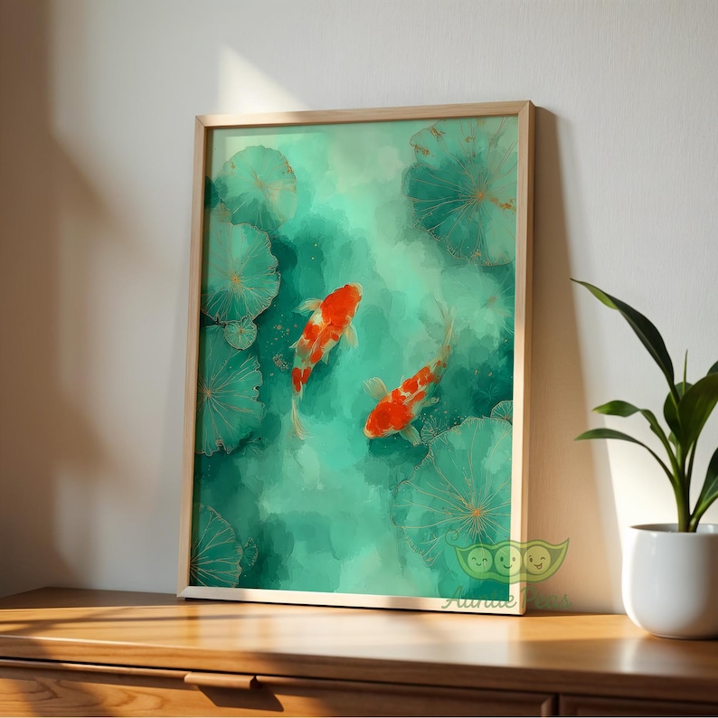 May include: A framed art print featuring two orange and white koi fish swimming in a teal pond with lily pads. The artwork has a watercolor style and is set in a light wooden frame. The print is displayed on a wooden surface.