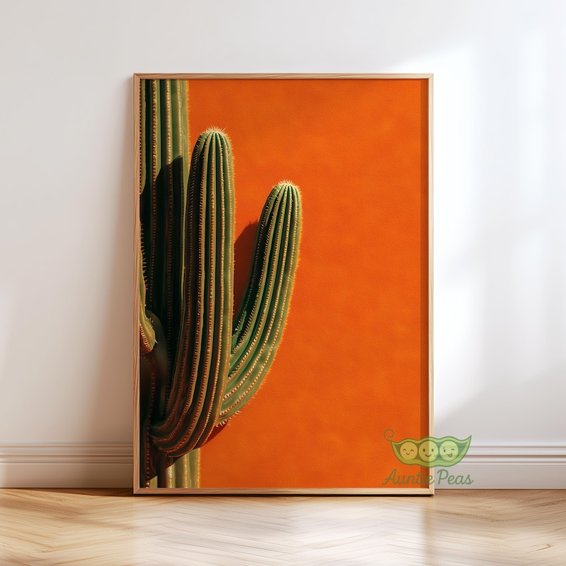 May include: A framed art print featuring a close-up of a green cactus against a vibrant orange background. The cactus has vertical ridges and small spines. The wooden frame adds a natural touch to the desert-themed artwork.