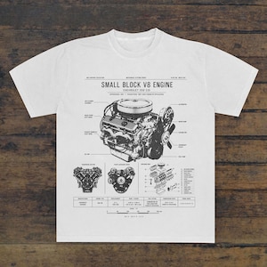May include: A white t-shirt featuring a black technical diagram of a Small Block V8 Engine. The graphic includes detailed labels, a transverse section, a front accessory drive, an exploded view, and a table with specifications like 350 CID.
