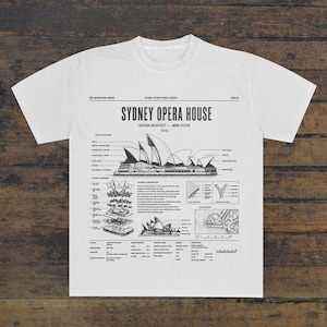 May include: A white t-shirt featuring a black architectural print of the Sydney Opera House. The graphic includes technical diagrams, structural details, site context, and text labels detailing the design architect, Jørn Utzon, and the year 1973.