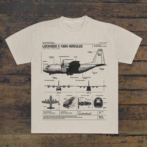 Może przedstawiać: Beżowy t-shirt z czarną grafiką techniczną przedstawiającą plan taktycznego samolotu transportowego Lockheed C-130H Hercules. Projekt zawiera wiele widoków, opisane komponenty oraz tekst historyczny szczegółowo opisujący specyfikację samolotu.