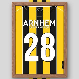 Op de afbeelding: Een ingelijste print met een geel en zwart gestreept patroon, met het woord "ARNHEM" in het wit. Het nummer "28" is groot en wit. De print bevat ook de tekst "ACHTER VITESSE" en "VITESSE".