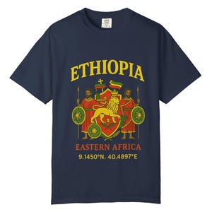 May include: Navy blue t-shirt featuring the word "ETHIOPIA" in yellow, above a graphic of a lion and two figures. The text "EASTERN AFRICA" and coordinates are below the graphic. The shirt is a classic crew neck.
