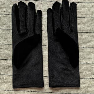 May include: A pair of black velvet gloves featuring a smooth, soft-touch fabric finish. The gloves have a classic five-finger design with a solid black color throughout, showcasing a consistent texture and a clean, straight-cut wrist opening.