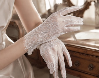May include: A pair of white lace gloves featuring a delicate floral pattern and scalloped edges. The gloves are crafted from a sheer, intricate mesh fabric that covers the hands and wrists, showcasing a detailed weave with visible floral motifs.