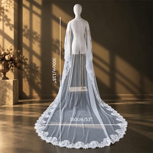 May include: A long white bridal veil with intricate lace trim along the edges, displayed on a mannequin. The veil measures 300cm/118 inches in length and 160cm/63 inches in width, featuring a sheer fabric that drapes to the floor in a train.