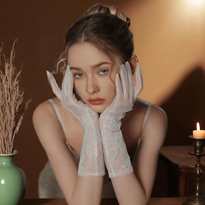 May include: Elegant white lace gloves with floral embroidery. The gloves are sheer and reach the mid-forearm. The delicate design adds a touch of vintage charm. Perfect for weddings, formal events, or adding a romantic flair to any outfit.