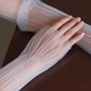 May include: Sheer white gloves with vertical pleated detailing. The gloves are made of a delicate, translucent fabric, and the design features a fingerless style. The fabric is lightweight and appears to be slightly textured.