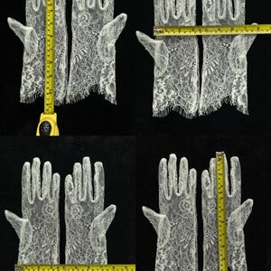 May include: A pair of white lace gloves with a floral pattern and scalloped edges. A yellow measuring tape shows the gloves are approximately 11 inches long and 3.5 inches wide at the palm area, providing clear scale for these delicate accessories.