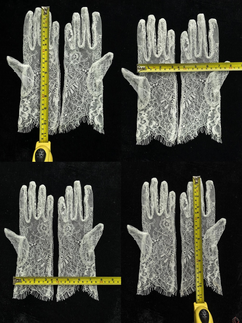 May include: A pair of white lace gloves with a floral pattern and scalloped edges. A yellow measuring tape shows the gloves are approximately 11 inches long and 3.5 inches wide at the palm area, providing clear scale for these delicate accessories.