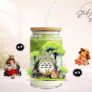 May include: A glass beverage container with a wooden lid and a glass straw, filled with a green liquid. The container is decorated with cartoon characters. The words "Cute and Creative Studio Sips Designs" are in a circle.