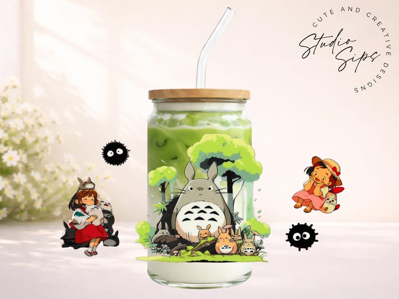 May include: A glass beverage container with a wooden lid and a glass straw, filled with a green liquid. The container is decorated with cartoon characters. The words "Cute and Creative Studio Sips Designs" are in a circle.