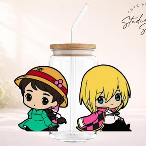 May include: Clear glass tumbler with a wooden lid and a curved glass straw. The tumbler features two cartoon character stickers. One character wears a green dress and a yellow hat with a red band. The other character has blonde hair and a pink and black cape. The text "Cute and Creative Studio Sips Designs" is in the upper right corner.