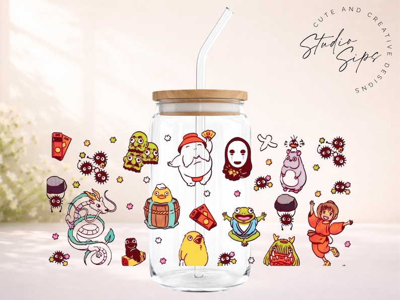 May include: A clear glass tumbler with a bamboo lid and a glass straw. The tumbler is decorated with colorful cartoon characters. The words "Cute and Creative Studio Sips Designs" are written in a script font.
