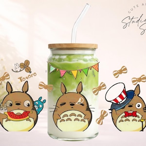 May include: A glass beverage container with a wooden lid and a straw, filled with a green drink. The container is decorated with Totoro cartoon characters and bow tie stickers. The text "Cute and Creative Designs" is visible.