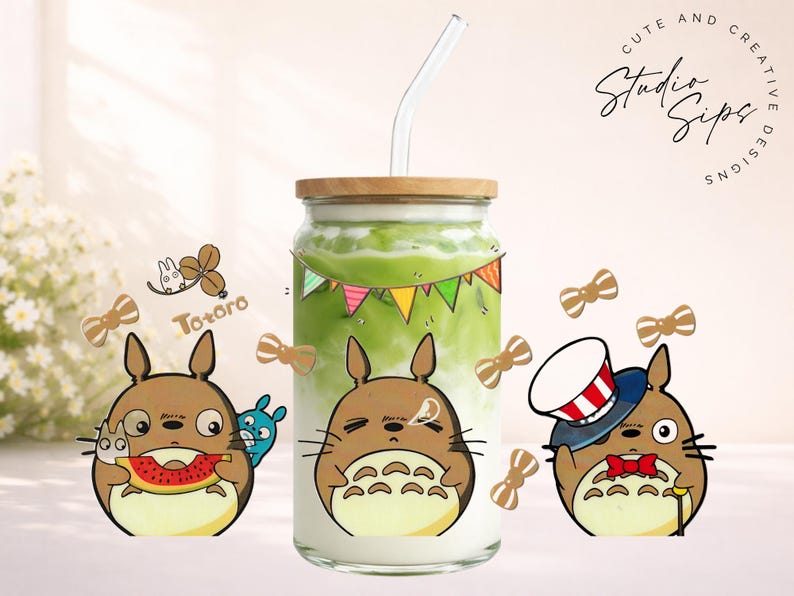 May include: A glass beverage container with a wooden lid and a straw, filled with a green drink. The container is decorated with Totoro cartoon characters and bow tie stickers. The text "Cute and Creative Designs" is visible.