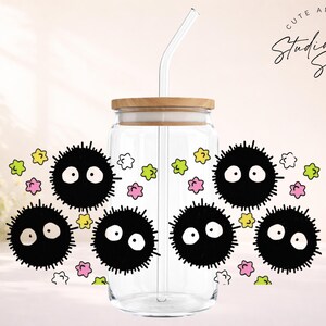 May include: Clear glass tumbler with a bamboo lid and a glass straw. The tumbler is decorated with black soot sprites and colorful star-shaped accents. The text "Cute and Creative Studio Sips Designs" is also visible.