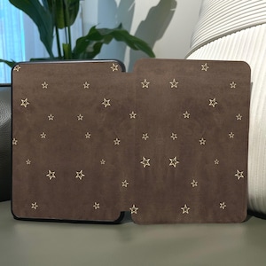 May include: A brown case with a black border and a matching cover. Both pieces are covered in small, gold star shapes. The case is rectangular with rounded corners. The cover has a cutout for easy access.