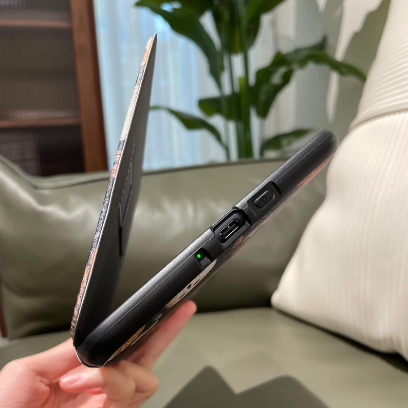 May include: Black phone case with a floral design and a matching flip cover. The case has a charging port and a power button. The flip cover is open, revealing the phone screen. The case is held in a person's hand.
