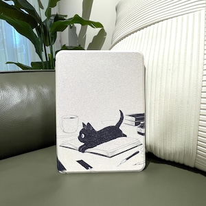 May include: A light-colored tablet case featuring a black cat illustration. The cat is lying on an open book, with a coffee cup, ink bottle, and pen also depicted. The case has a smooth, matte finish.