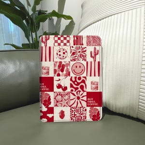 May include: A red and white patterned phone case featuring various designs, including a disco ball, smiley face, and cactus. The text "BUT FIRST, COFFEE" is also displayed on the case. The case is rectangular and appears to be made of a hard material.