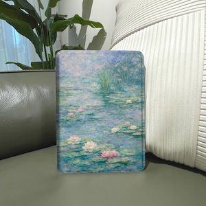 Könnte beinhalten: Eine rechteckige E-Reader-Hülle mit einem gedruckten Abbild eines Seerosenteich-Gemäldes. Das Kunstwerk zeigt eine ruhige Wasserlandschaft mit sanften blauen, grünen und rosafarbenen Pinselstrichen, die schwimmende Seerosen und Blüten darstellen.