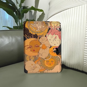 May include: A rectangular tablet case featuring a celestial-themed print with multiple cats, suns, moons, and stars in shades of orange, yellow, cream, and black. The design includes stylized feline figures interacting with crescent moons and sun faces.