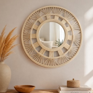 May include: A round wall mirror featuring a light beige rattan frame with a sunburst-inspired design. The frame consists of concentric circles connected by radiating spokes, surrounding a central circular glass mirror surface.
