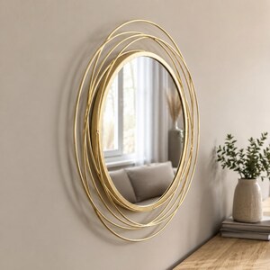 Peut inclure: Un miroir mural rond dot&eacute; d'un cadre dor&eacute; compos&eacute; de plusieurs anneaux m&eacute;talliques fins superpos&eacute;s. Le miroir central en verre circulaire est entour&eacute; d'un design complexe en fil m&eacute;tallique superpos&eacute; cr&eacute;ant une impression de profondeur.