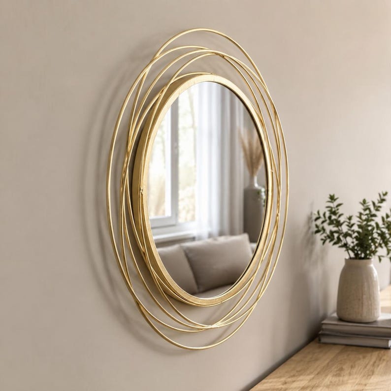 Peut inclure: Un miroir mural rond dot&eacute; d'un cadre dor&eacute; compos&eacute; de plusieurs anneaux m&eacute;talliques fins superpos&eacute;s. Le miroir central en verre circulaire est entour&eacute; d'un design complexe en fil m&eacute;tallique superpos&eacute; cr&eacute;ant une impression de profondeur.