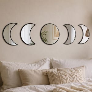 May include: A set of five wall-mounted mirrors featuring black frames. The arrangement includes two crescent moon shapes on the left, a central circular mirror, and two additional crescent moon shapes on the right, depicting the lunar cycle phases.