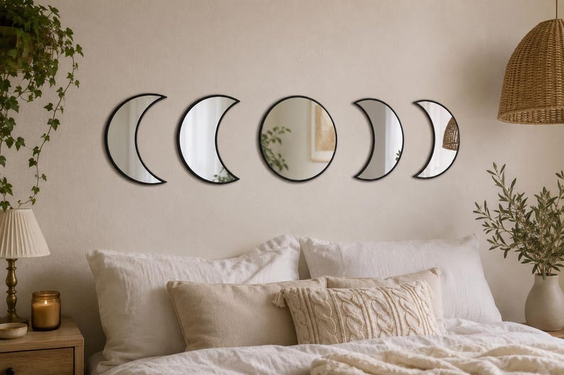 May include: A set of five wall-mounted mirrors featuring black frames. The arrangement includes two crescent moon shapes on the left, a central circular mirror, and two additional crescent moon shapes on the right, depicting the lunar cycle phases.