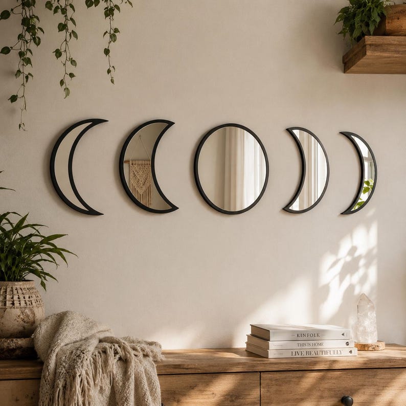 May include: A set of five wall-mounted mirrors featuring black frames arranged to represent the phases of the moon. The collection includes one circular mirror in the center, flanked by two crescent mirrors on each side, all with reflective glass.
