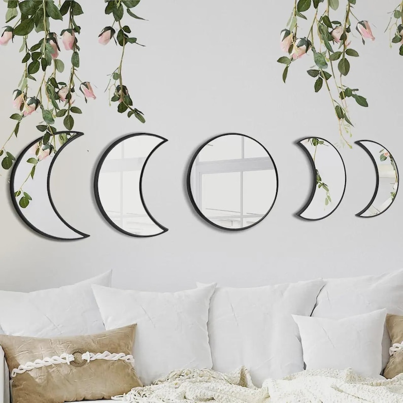 May include: A set of five wall-mounted mirrors with black frames, arranged to display the phases of the moon. The collection includes one circular mirror in the center, flanked by two crescent moon mirrors and two smaller crescent moon mirrors.