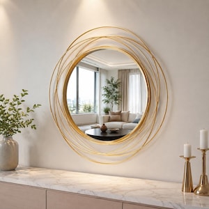 Peut inclure: Un miroir mural rond dot&eacute; d'un cadre dor&eacute; compos&eacute; de plusieurs anneaux circulaires fins superpos&eacute;s. La vitre centrale circulaire offre un reflet clair de l'int&eacute;rieur d'un salon, incluant un canap&eacute;, une table basse et une fen&ecirc;tre.