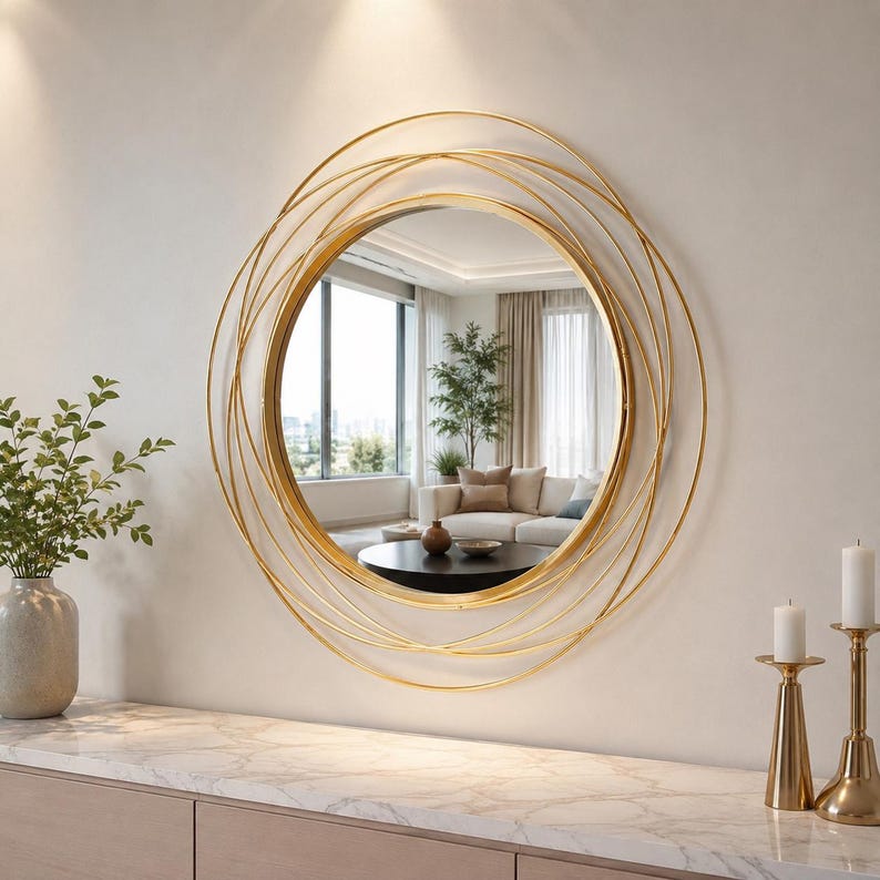 Peut inclure: Un miroir mural rond dot&eacute; d'un cadre dor&eacute; compos&eacute; de plusieurs anneaux circulaires fins superpos&eacute;s. La vitre centrale circulaire offre un reflet clair de l'int&eacute;rieur d'un salon, incluant un canap&eacute;, une table basse et une fen&ecirc;tre.