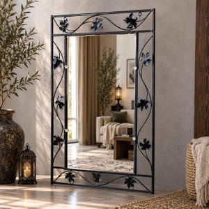 May include: A rectangular wall mirror featuring a black metal frame with decorative wrought iron vine and leaf accents. The frame includes thin, curved metal bars that extend along the sides, adorned with small, dark metal leaves.