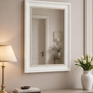 Pode incluir: Um espelho de parede retangular com uma moldura de madeira espessa pintada de branco e uma borda interna fina em tom dourado. O vidro do espelho é claro e reflexivo, apresentando um design clássico e limpo com bordas chanfradas na moldura.