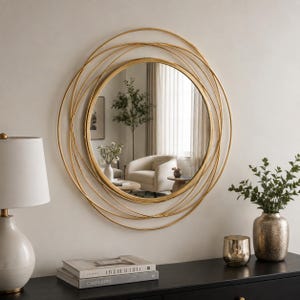 Peut inclure: Un miroir mural rond dot&eacute; d'un cadre dor&eacute; compos&eacute; de plusieurs anneaux m&eacute;talliques fins et circulaires qui se chevauchent. Le miroir central en verre refl&egrave;te l'int&eacute;rieur d'une pi&egrave;ce avec un fauteuil, une plante et des rideaux superpos&eacute;s.