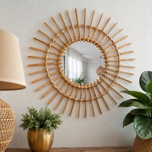May include: A round wall mirror featuring a sunburst frame constructed from light brown natural rattan reeds. The circular glass center is surrounded by a woven rattan border, with straight reed spokes radiating outward in a sun-like pattern.