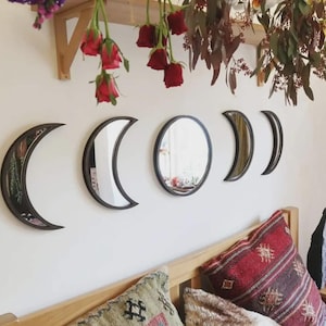 May include: A set of five wall-mounted mirrors arranged in a horizontal row to represent the phases of the moon. The mirrors feature dark frames and include two crescent shapes, two partial moon shapes, and one circular mirror in the center.