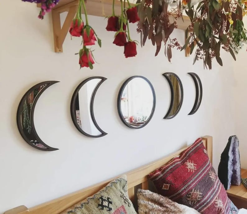 May include: A set of five wall-mounted mirrors arranged in a horizontal row to represent the phases of the moon. The mirrors feature dark frames and include two crescent shapes, two partial moon shapes, and one circular mirror in the center.