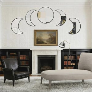 May include: A set of five wall-mounted mirrors arranged in a horizontal lunar phase sequence. The collection includes one central circular mirror flanked by four crescent-shaped mirrors, all featuring thin black frames and reflective glass surfaces.