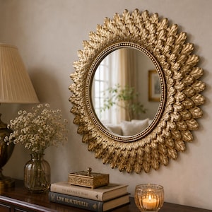 Puede incluir: Un espejo de pared redondo con un marco decorativo compuesto por múltiples capas de elementos dorados en forma de hoja dispuestos en un patrón de rayos de sol. El cristal circular central está bordeado por un fino ribete dorado con cuentas.