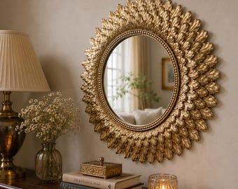 Peut inclure: Un miroir mural rond doté d'un cadre décoratif composé de plusieurs couches d'éléments dorés en forme de feuilles disposés en rayons de soleil. Le verre circulaire central est bordé d'une fine garniture perlée dorée, créant un aspect texturé.
