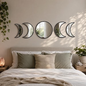 May include: A set of five wall-mounted mirrors featuring black frames arranged in a horizontal line. The collection includes one large circular mirror in the center, flanked by two pairs of crescent moon-shaped mirrors of varying sizes.