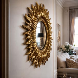 Könnte beinhalten: Ein ovaler Wandspiegel mit einem markanten goldfarbenen Rahmen in einem strukturierten, strahlenförmigen Design. Der Rahmen besteht aus zahlreichen geschwungenen, flammenartigen Vorsprüngen, die von der zentralen Spiegelfläche ausgehen.